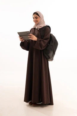 أهمية التعليم في المجتمع السعودي, استخدام الأجهزة التقنية الحديثة والمتطورة, الدراسة اون لاين عبر الجهاز اللوحي ,  بورتريه لامرأة عربية خليجية سعودية محجبة ترتدي العباءة وتحمل حقيبة الظهر تعمل على جهاز الحاسوب المحمول, الجسم بالطول الكامل، خلفية بيضاء