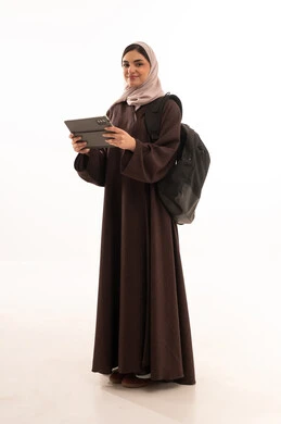 استخدام الأجهزة التقنية الحديثة والمتطورة, الدراسة اون لاين عبر الجهاز اللوحي ,  بورتريه لامرأة عربية خليجية سعودية محجبة ترتدي العباءة وتحمل حقيبة الظهر تعمل على جهاز الحاسوب المحمول, شابة سعودية تقوم بإنجاز المهام, الجسم بالطول الكامل، خلفية بيضاء