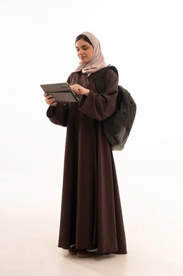 Online study via tablet, using modern and advanced technological devices, a portrait of a Saudi Arabian Gulf woman wearing a hijab and an abaya, carrying a backpack and working on a laptop, a young Saudi woman completing tasks, full-body, white background.