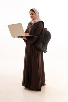 التصفح عبر الجهاز المحمول الحاسب, استخدام الأجهزة التقنية الحديثة والمتطورة, بورتريه لامرأة عربية خليجية سعودية محجبة ترتدي العباءة وتحمل حقيبة الظهر تعمل على جهاز الحاسوب المحمول, شابة سعودية تقوم بإنجاز المهام, الجسم بالطول الكامل، خلفية بيضاء