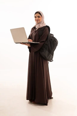 مفهوم العمل عن بعد, استخدام الأجهزة التقنية الحديثة والمتطورة, بورتريه لامرأة عربية خليجية سعودية محجبة ترتدي العباءة وتحمل حقيبة الظهر تعمل على جهاز الحاسوب المحمول, شابة سعودية تقوم بإنجاز المهام, الجسم بالطول الكامل، خلفية بيضاء