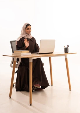 القاء التحية عبر مكالمة فيديو،الأجهزة التقنية الحديثة بالتعلم,، متابعة المحاضرات عن طريق منصات التعلم، بورتريه لطالبه عربيه خليجيه سعودية ترتدي الحجاب والعباءة تجلس على الطاولة المكتبيه ، حل الواجبات وتلقي المحاضرات المدرسيه عن بعد عبر التابلت، خلفية بيضاء