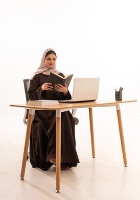 قراءة الملاحظات وتدوينها على الحاسب،الأجهزة التقنية الحديثة بالتعلم,، متابعة المحاضرات عن طريق منصات التعلم، بورتريه لطالبه عربيه خليجيه سعودية ترتدي الحجاب والعباءة تجلس على الطاولة المكتبيه ، حل الواجبات وتلقي المحاضرات المدرسيه عن بعد عبر التابلت، خلفية بيضاء