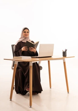 ايماءات السرور والفرح،الأجهزة التقنية الحديثة بالتعلم,، متابعة المحاضرات عن طريق منصات التعلم، بورتريه لطالبه عربيه خليجيه سعودية ترتدي الحجاب والعباءة تجلس على الطاولة المكتبيه ، حل الواجبات وتلقي المحاضرات المدرسيه عن بعد عبر التابلت، خلفية بيضاء