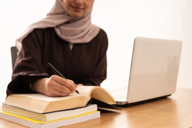 Writing and taking notes during the lecture, modern technological devices in learning, following lectures through learning platforms, a close-up portrait of a Gulf Arab Saudi female student wearing a hijab and abaya sitting at a desk, university lectures remotely via tablet, white background.