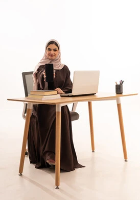 عرض خلفية سوداء على الهاتف المحمول، المحاضرات الجامعية عن بعد عبر الحاسب، الأجهزة التقنية الحديثة بالتعلم,، متابعة المحاضرات عن طريق منصات التعلم، بورتريه مقرب لطالبه عربيه خليجيه سعودية ترتدي الحجاب والعباءة تجلس على الطاولة المكتبيه ، خلفية بيضاء