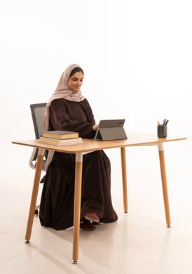 استخدام التابلت في الدراسة، المحاضرات الجامعية عن بعد عبر الحاسب، الأجهزة التقنية الحديثة بالتعلم,، متابعة المحاضرات عن طريق منصات التعلم، بورتريه مقرب لطالبه عربيه خليجيه سعودية ترتدي الحجاب والعباءة تجلس على الطاولة المكتبيه ، خلفية بيضاء