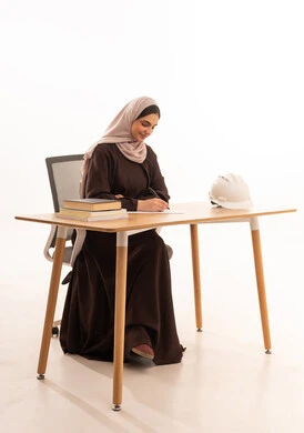 Writing memories of the educational journey, an architecture student attending university lectures remotely via a tablet, modern technological devices in learning, a close-up portrait of an Arab Gulf Saudi female student wearing a hijab and abaya sitting at a desk, white background.
