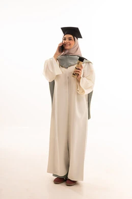 اتصال هاتفي في يوم التخرج، إيماءات السعادة بالوصول الى الحلم، النجاح والتفوق والتخرج من الجامعة، الاحتفال بإنهاء الدراسة الجامعية، النظر الى الكاميرا بايماءات الفخر، بورتريه لخريجة عربية خليجية سعودية محجبة ترتدي زي التخرج والقبعة تحمل بيدها الشهادة، خلفية بيضاء
