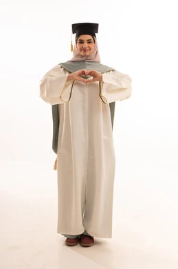 حركة يدين على شكل قلب، إيماءات السعادة بالوصول الى الحلم، النجاح والتفوق والتخرج من الجامعة، الاحتفال بإنهاء الدراسة الجامعية، النظر الى الكاميرا بايماءات الفخر، بورتريه لخريجة عربية خليجية سعودية محجبة ترتدي زي التخرج والقبعة ، خلفية بيضاء