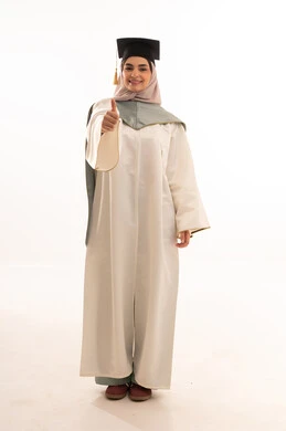 Raising the thumb with a sign of approval, gestures of happiness at reaching the dream, success and excellence and graduating from university, celebrating the completion of university studies, looking at the camera with gestures of pride, a portrait of a Saudi Gulf Arab female graduate wearing graduation attire and cap, with a white background.