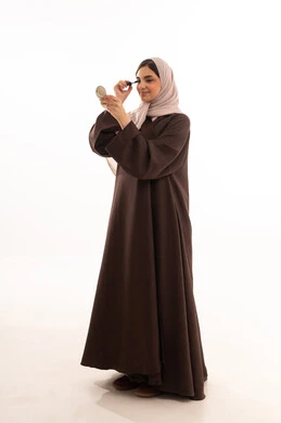 مفهوم العناية بالجمال والبشرة,  استخدام المساحيق التجميلية, مفهوم التزين والتجمل,  التسويق لمستحضرات ومنتجات التجميل, الاهتمام والعناية بالمظهر الخارجي,  بورتريه لامرأة عربية خليجية سعودية محجبة ترتدي العباءة السوداء تستعمل فرشاة المسكارة, خلفية بيضاء