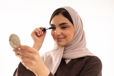 استخدام المساحيق التجميلية, مفهوم التزين والتجمل,  التسويق لمستحضرات ومنتجات التجميل, الاهتمام والعناية بالمظهر الخارجي, استخدام المساحيق التجميلية, بورتريه مقرب لامرأة عربية خليجية سعودية محجبة ترتدي العباءة السوداء تستعمل فرشاة المسكارة, خلفية بيضاء