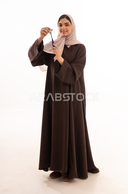 Beauty and skin care, the use of cosmetics, the concept of adornment and beautification, marketing of cosmetic products, attention and care for the external appearance, a portrait of a Saudi Arabian Gulf woman wearing a black abaya and using a mascara brush, white background.