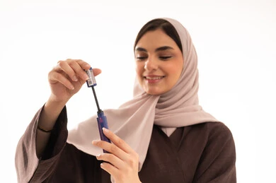 العناية بالمظهر الخارجي, استخدام المساحيق التجميلية, مفهوم التزين والتجمل,  التسويق لمستحضرات ومنتجات التجميل, الاهتمام والعناية بالمظهر الخارجي,  بورتريه مقرب لامرأة عربية خليجية سعودية محجبة ترتدي العباءة السوداء تستعمل فرشاة المسكارة, خلفية بيضاء