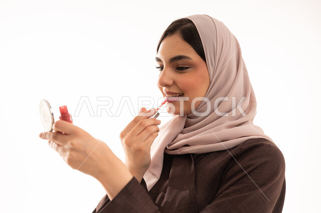 التعرف على منتجات الشفاه، استخدام المساحيق التجميلية, مفهوم التزين والتجمل,  التسويق لمستحضرات ومنتجات التجميل, الاهتمام والعناية بالمظهر الخارجي,  بورتريه مقرب لامرأة عربية خليجية سعودية محجبة ترتدي العباءة السوداء تستعمل أحمر الشفاه, خلفية بيضاء