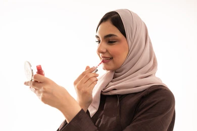 التعرف على منتجات الشفاه، استخدام المساحيق التجميلية, مفهوم التزين والتجمل,  التسويق لمستحضرات ومنتجات التجميل, الاهتمام والعناية بالمظهر الخارجي,  بورتريه مقرب لامرأة عربية خليجية سعودية محجبة ترتدي العباءة السوداء تستعمل أحمر الشفاه, خلفية بيضاء