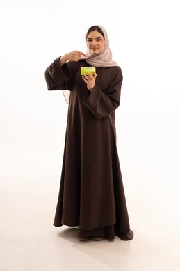 Using the best creams for moisturizing, using cosmetics, the concept of adornment and beautification, marketing of cosmetic products, attention and care for the external appearance, a portrait of a Saudi Arabian Gulf woman wearing a black abaya and using a moisturizing cream, white background.