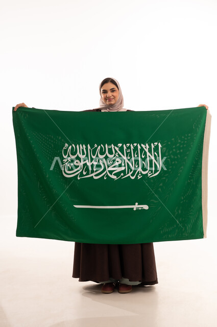 ساليوم الوطني السعودي، المشاركة الأعياد الوطنية، بورتريه لامرأة عربية خليجية سعودية محجبة مبتسمة ترتدي الحجاب وترفع علم السعودية بايماءات الفخر والاعتزاز بالوطن، يوم العلم السعودي 11 مارس، العيد الوطني 23 سبتمبر، صورة الجسم بالطول الكامل، خلفية بيضاء