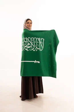 Pride and honor in belonging to the homeland, commemorating the Saudi National Day on September 23, Flag Day on March 11, celebrating national occasions, raising the banner of monotheism and Islam, a portrait of a Saudi Gulf Arab woman in a hijab holding the green Saudi flag in her hand, full-body, white background.