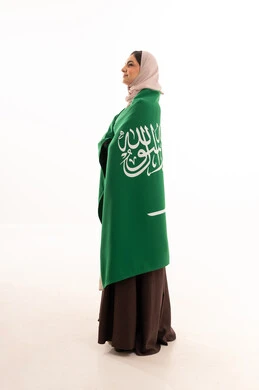 Pride and honor in belonging to the homeland, commemorating the Saudi National Day on September 23, Flag Day on March 11, celebrating national occasions, raising the banner of monotheism and Islam, a portrait of a Saudi Gulf Arab woman in a hijab holding the green Saudi flag in her hand, full-body, white background.