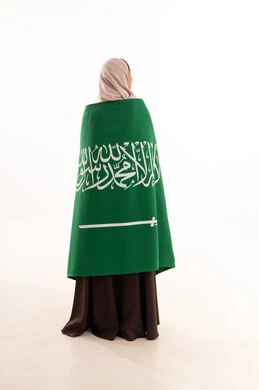 Celebrating national occasions, pride and honor in belonging to the homeland, commemorating Saudi National Day on September 23, Flag Day on March 11, raising the banner of monotheism and Islam, a portrait from behind of a Saudi Arabian Gulf woman wearing a hijab holding the Saudi flag in her hand, full-body, white background.