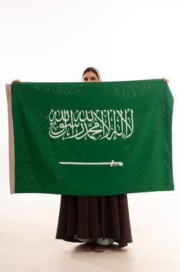 Commemoration of the Saudi National Day on September 23, Flag Day on March 11, celebration of national occasions, raising the banner of monotheism and Islam, a portrait of a Saudi Gulf Arab woman in a hijab holding the green Saudi flag in her hand, pride and honor in belonging to the homeland, full-body image, white background.