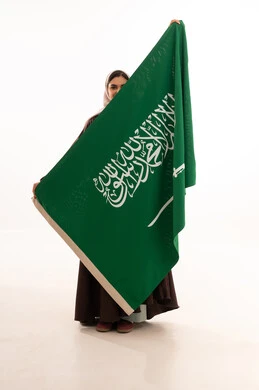 استذكار اليوم الوطني السعودي 23 سبتمبر، يوم العلم 11 مارس، الاحتفال بالمناسبات الوطنية، رفع راية التوحيد والإسلام، بورتريه لامرأة عربية خليجية سعودية محجبة تحمل بيدها علم السعودية الاخضر، الفخر و الاعتزاز بالانتماء للوطن، الجسم بالطول الكامل، خلفية بيضاء