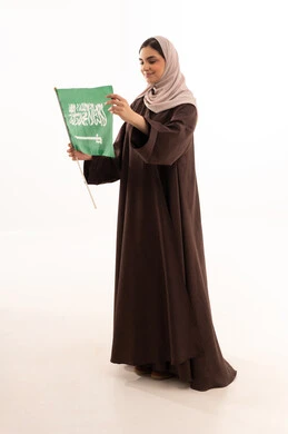 Raising the banner of monotheism and Islam, celebrating national occasions, pride and honor in belonging to the homeland, commemorating Saudi National Day on September 23, Flag Day on March 11, a portrait of a Saudi Arabian Gulf woman in a hijab holding the Saudi flag in her hand, full body length, white background.