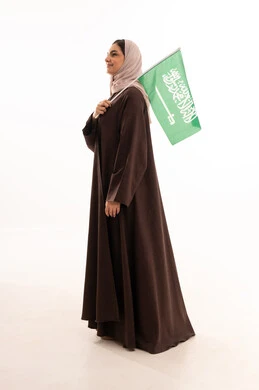 Pride in the country's achievements, raising the banner of monotheism and Islam, celebrating national occasions, pride in belonging to the homeland, commemorating Saudi National Day on September 23, Flag Day on March 11, a portrait of a Saudi Gulf Arab woman in a hijab holding the Saudi flag in her hand, full body length, white background.