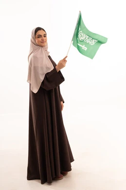 Raising the banner of monotheism and Islam, celebrating national occasions, pride and honor in belonging to the homeland, commemorating Saudi National Day on September 23, Flag Day on March 11, a portrait of a Saudi Arabian Gulf woman in a hijab holding the Saudi flag in her hand, full body length, white background.