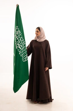 رفع راية التوحيد والإسلام، الاحتفال بالمناسبات الوطنية، الفخر و الاعتزاز بالانتماء للوطن، استذكار اليوم الوطني السعودي 23 سبتمبر، يوم العلم 11 مارس، بورتريه لامرأة عربية خليجية سعودية محجبة تحمل بيدها علم السعودية ، الطول الكامل للجسم، خلفية بيضاء