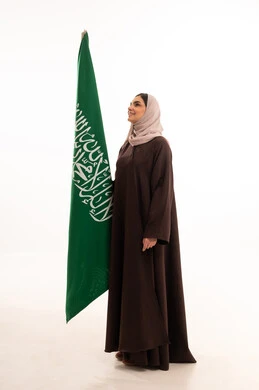 الفخر بإنجازات البلاد، رفع راية التوحيد والإسلام، الاحتفال بالمناسبات الوطنية،  الاعتزاز بالانتماء للوطن، استذكار اليوم الوطني السعودي 23 سبتمبر، يوم العلم 11 مارس، بورتريه لامرأة عربية خليجية سعودية محجبة تحمل بيدها علم السعودية ، الطول الكامل للجسم، خلفية بيضاء