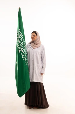 الاحتفال بالمناسبات الوطنية، استذكار اليوم الوطني السعودي 23 سبتمبر، يوم العلم 11 مارس، إعمار البلاد بسواعد ابنائه، رفع راية التوحيد والإسلام، بورتريه لطبيبة عربية خليجية سعودية محجبة ترتدي المعطف الطبي تحمل بيدها علم السعودية ، الطول الكامل للجسم، خلفية بيضاء