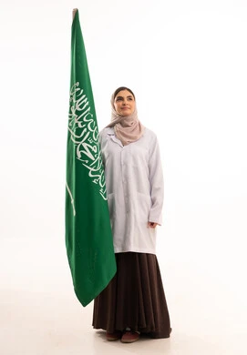 Commemoration of the Saudi National Day on September 23, Flag Day on March 11, the reconstruction of the country by the hands of its sons, raising the banner of monotheism and Islam, celebrating national occasions, a portrait of a veiled Arab Gulf Saudi female doctor wearing a medical coat holding the Saudi flag in her hand, full body length, white background.