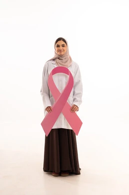 Clarification of the importance of early screening in October, the concept of medicine and healthcare, a portrait of an Arab Gulf Saudi female doctor wearing an abaya and a white coat holding a flag with the breast cancer awareness symbol, a pink ribbon in awareness campaigns, full body length, white background.
