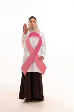 Raising the hand with gestures to request a stop, explaining the importance of early detection in October, the concept of medicine and healthcare, a portrait of an Arab Gulf Saudi female doctor wearing an abaya and a white coat holding a pink ribbon symbolizing breast cancer awareness, full body length, white background.