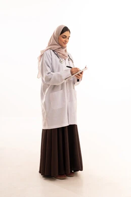 مفهوم الطب والرعاية الصحية، العمل في القطاع الصحي، بورتريه لطبيبة عربية خليجية سعودية محجبة ترتدي عباءه ملونة مع المعطف الطبي تقوم بتدوين وتسجيل معلومات المرضى, تقديم الخدمات العلاجية في المراكز الطبية والمستشفيات، صورة الجسم بالطول الكامل، خلفيه بيضاء