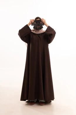 استخدام مكون  ومستحضر تجميلي، خطوات تنظيف وتقشير البشرة، مفهوم العناية والاهتمام بالمظهر الخارجي عند النساء، بورتريه لامرأة عربية خليجية سعودية ترتدي العباءة تقوم بوضع قناع الطين على وجهها، صورة الجسم بالكامل، خلفية بيضاء