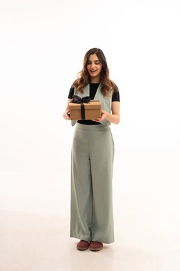 الاحتفال بأعياد الميلاد, التعبير عن المحبة والتقدير,تقديم الهدايا في المناسبات السعيدة,  بورتريه لامرأة عربية خليجية سعودية  ترتدي اللباس الكاجوال  تمسك بيديها علبة هداية, شابة سعودية تنظر إلى الكاميرا بإيماءات السعادة والسرور, الجسم بالطول الكامل، خلفية بيضاء