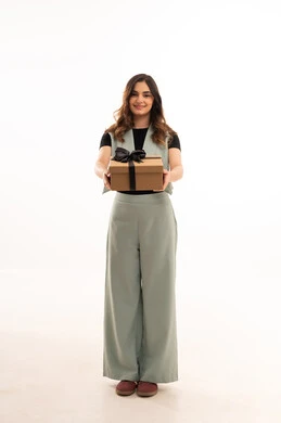 تقديم الهدايا في المناسبات السعيدة, الاحتفال بأعياد الميلاد, التعبير عن المحبة والتقدير, بورتريه لامرأة عربية خليجية سعودية  ترتدي اللباس الكاجوال  تمسك بيديها علبة هداية, شابة سعودية تنظر إلى الكاميرا بإيماءات السعادة والسرور, الجسم بالطول الكامل، خلفية بيضاء