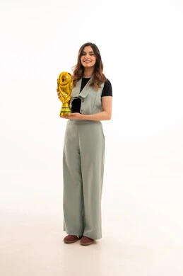 ايماءات الفوز والنصر، كأس العالم ذهبي لامع،الاهتمام بالمظهر الخارجي والأناقة، بورتريه لإمرأة عربية خليجية سعودية ترتدي زي الكاجوال  تمسك بيدها كأس العالم ، خلفية بيضاء