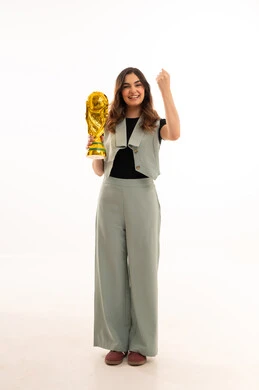 ايماءات الفوز والنصر، كأس العالم ذهبي لامع،الاهتمام بالمظهر الخارجي والأناقة، بورتريه لإمرأة عربية خليجية سعودية ترتدي زي الكاجوال  تمسك بيدها كأس العالم ، خلفية بيضاء