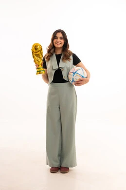 كأس العالم ذهبي لامع،الاهتمام بالمظهر الخارجي والأناقة،ايماءات الفوز والنصر،  بورتريه لإمرأة عربية خليجية سعودية ترتدي زي الكاجوال  تمسك بيدها كأس العالم و اليد الثانية كرة القدم، خلفية بيضاء