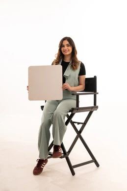 لوحات توضيحية ووسائل تعليمية، العروض والإعلانات التسويقية, بورتريه لشابة عربية خليجية سعودية ترتدي الزي الكاجوال تجلس على الكرسي  تمسك بيديها لوحة بيضاء مستطيلة فارغة ، النظر إلى الكاميرا بتعابير السعادة والسرور، خلفية بيضاء