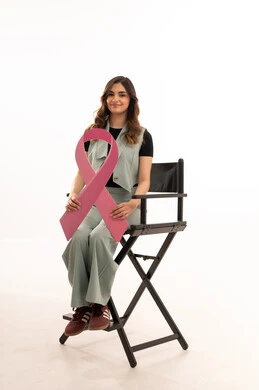 الحملة التوعيه بالامراض الخبيثة, بورتريه لشابة عربية خليجية سعودية مبتسمة ترتدي الزي الكاجوال تمسك بيدها شعار التوعيه للكشف المبكر عن سرطان الثدي، خلفية بيضاء