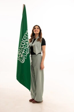 Pride and honor in national identity, a portrait of a young Arab Gulf Saudi woman wearing casual attire holding the Kingdom's flag with gestures of joy and happiness, celebrating Saudi Flag Day on March 11, commemorating the National Day for the unification of Saudi Arabia, Saudi National Day on the 8th of Rabi' al-Awwal, white background.