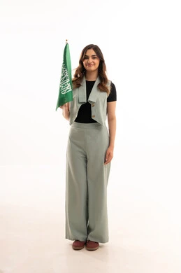 Celebrating Saudi Flag Day on March 11, pride and honor in national identity, a portrait of a young Arab Gulf Saudi woman wearing casual attire holding the Kingdom's flag with gestures of joy and happiness, commemorating the National Day for the unification of Saudi Arabia, the Saudi National Day on the 8th of Rabi' al-Awwal, white background.
