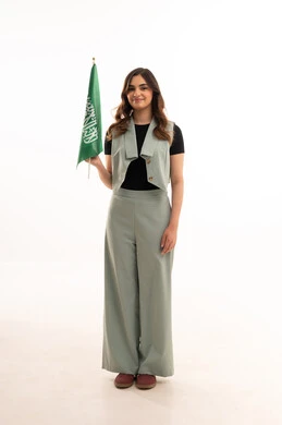 الفخر والاعتزاز بالهوية الوطنية، بورتريه لشابة عربية خليجية سعودية ترتدي الزي الكاجوال تحمل علم المملكة بإيماءات السرور والسعادة، الاحتفال بيوم العلم السعودي 11 مارس، احياء ذكرى اليوم الوطني  لتوحيد السعودية، العيد الوطني السعودي 8 ربيع الأول، خلفية بيضاء