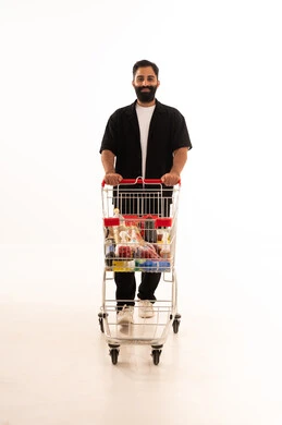 بورتريه لرجل عربي خليجي عماني يرتدي الزي الكاجوال يقف و عربة المشتريات أمامه ، شراء المستلزمات والحاجيات الضرورية، الاستمتاع بالتسوق في المولات والمراكز التجارية، الاستفادة من الخصومات والتنزيلات على المنتجات، الجسم بالطول الكامل، خلفية بيضاء